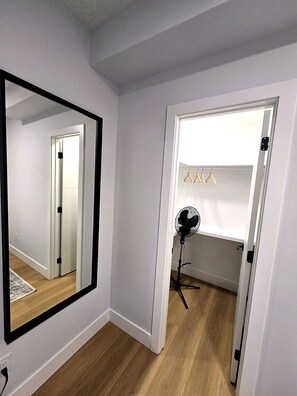 Une pièce dotée d’un grand miroir, d’un ventilateur sur pied et d’une porte donnant sur un placard où sont suspendus des vêtements.