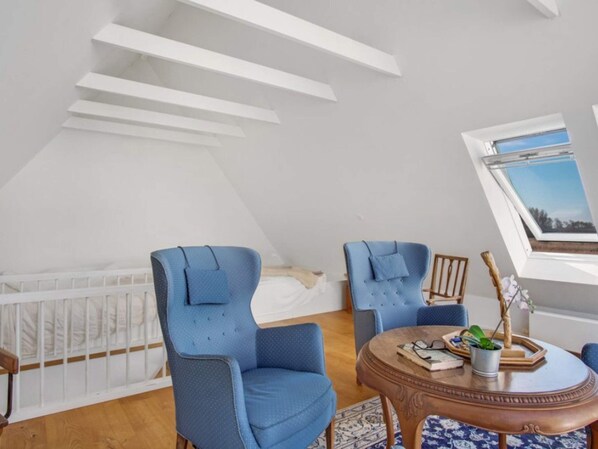 A room with a sloped ceiling, two blue chairs, a wooden table with a tray, and a window with a view. - 4 Person Holiday Home in Sejero (Sejero)