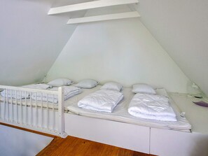 A small, white, single-bed room with a sloped ceiling and a white crib.