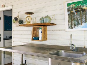 A kitchen with a stainless steel sink, wooden shelf with glass jars, and a painting of trees.