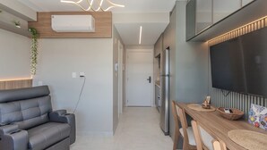 Ett modernt kök med inbyggd luftkonditionering, en matplats med ett träbord och stolar samt en grå soffa.
