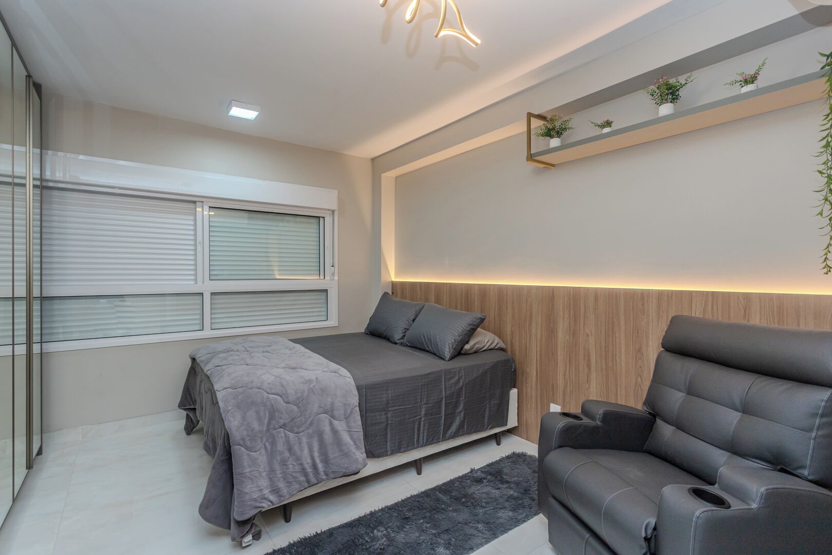Une chambre moderne avec un lit, un canapé, une fenêtre avec des stores, une étagère avec des plantes et un luminaire au plafond.
