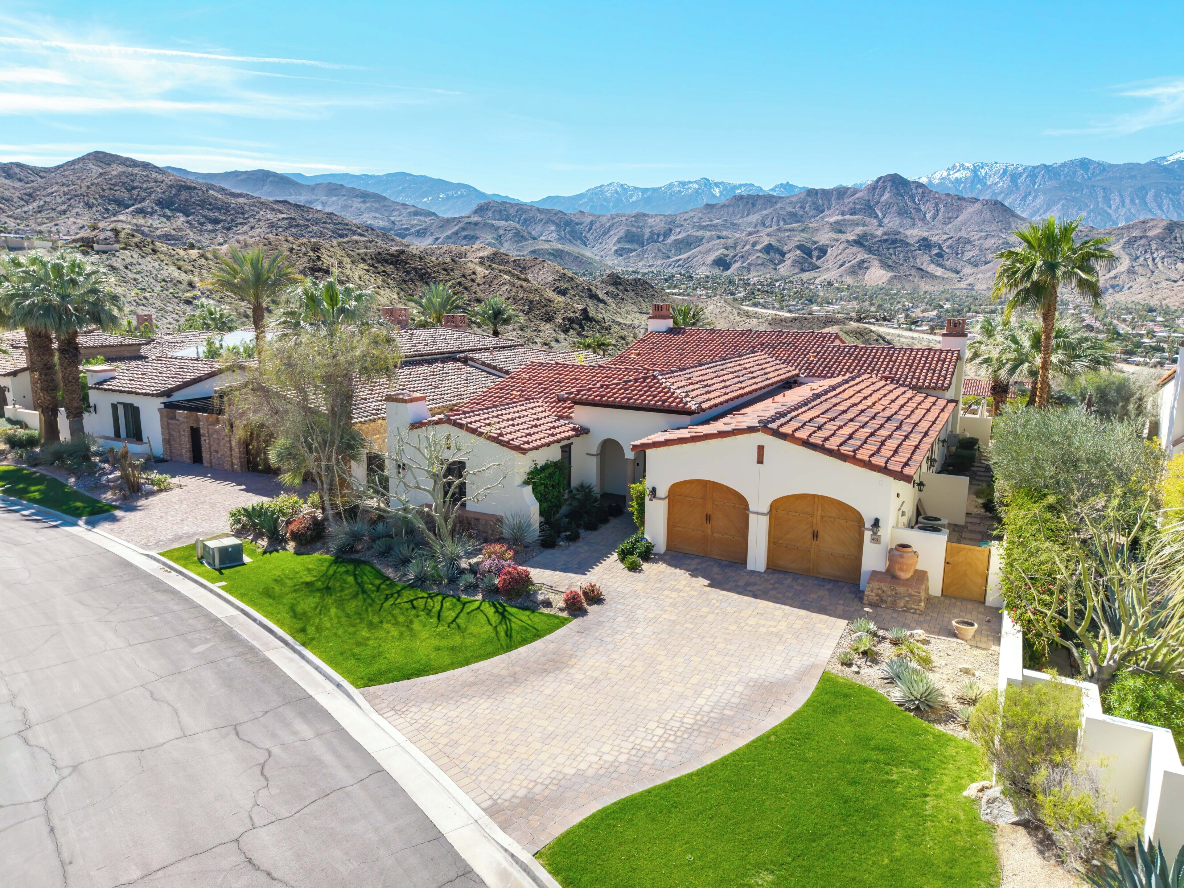 Zona residencial con casas de techo rojo, rodeada de montañas y palmeras.