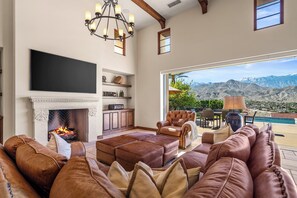 Ein geräumiges Wohnzimmer mit Kamin, Ledersofas, Fernseher und Bergblick.