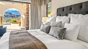 Een slaapkamer met een groot bed, uitzicht op bergen en een terras met een zwembad.