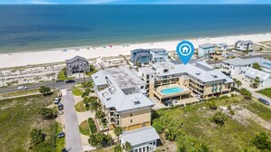 Vista aérea de un hotel frente al mar, con varias construcciones, una piscina y una playa al fondo.