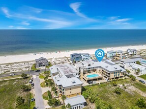 An aerial view of a coastal hotel with multiple buildings, a swimming pool, and a beach in the background. - The Club at Mexico Beach, 3BD/2BA, panoramic gulf views, steps to the beach, community pool! (Mexico Beach)
