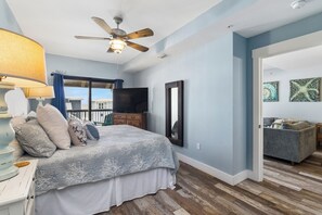 Un dormitorio con cama, ventilador de techo, televisor, cómoda y vistas al exterior.