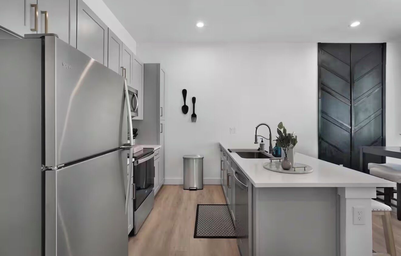 A modern kitchen with stainless steel appliances, a white countertop, and a black trash bin.