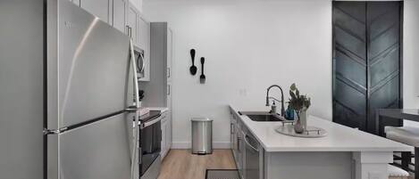 A modern kitchen with stainless steel appliances, a white countertop, and a black trash bin.