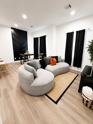 A modern living room with a sectional sofa, a dining table, and black curtains. -  Houston Heights 3 Beds + Garage (Houston)