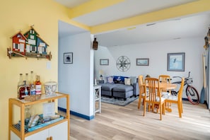 A living room with a sofa, dining table, chairs, a bicycle, and a wall-mounted shelf with bottles and a framed certificate.
