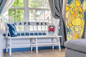 A white bench with 'CAPE MAY' signage, a pillow with a crab design, and a colorful abstract wall.