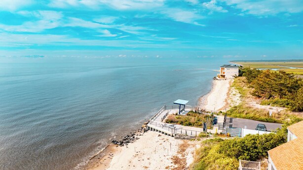 Una propiedad costera con playa, muelle y casa con balcón con vistas al mar.