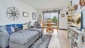Una sala de estar con un sofá seccional gris, un comedor con sillas de madera, una bicicleta y un televisor sobre un soporte de madera.