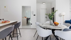 Una cocina moderna con comedor, paredes blancas y una puerta visible que da a otra habitación.