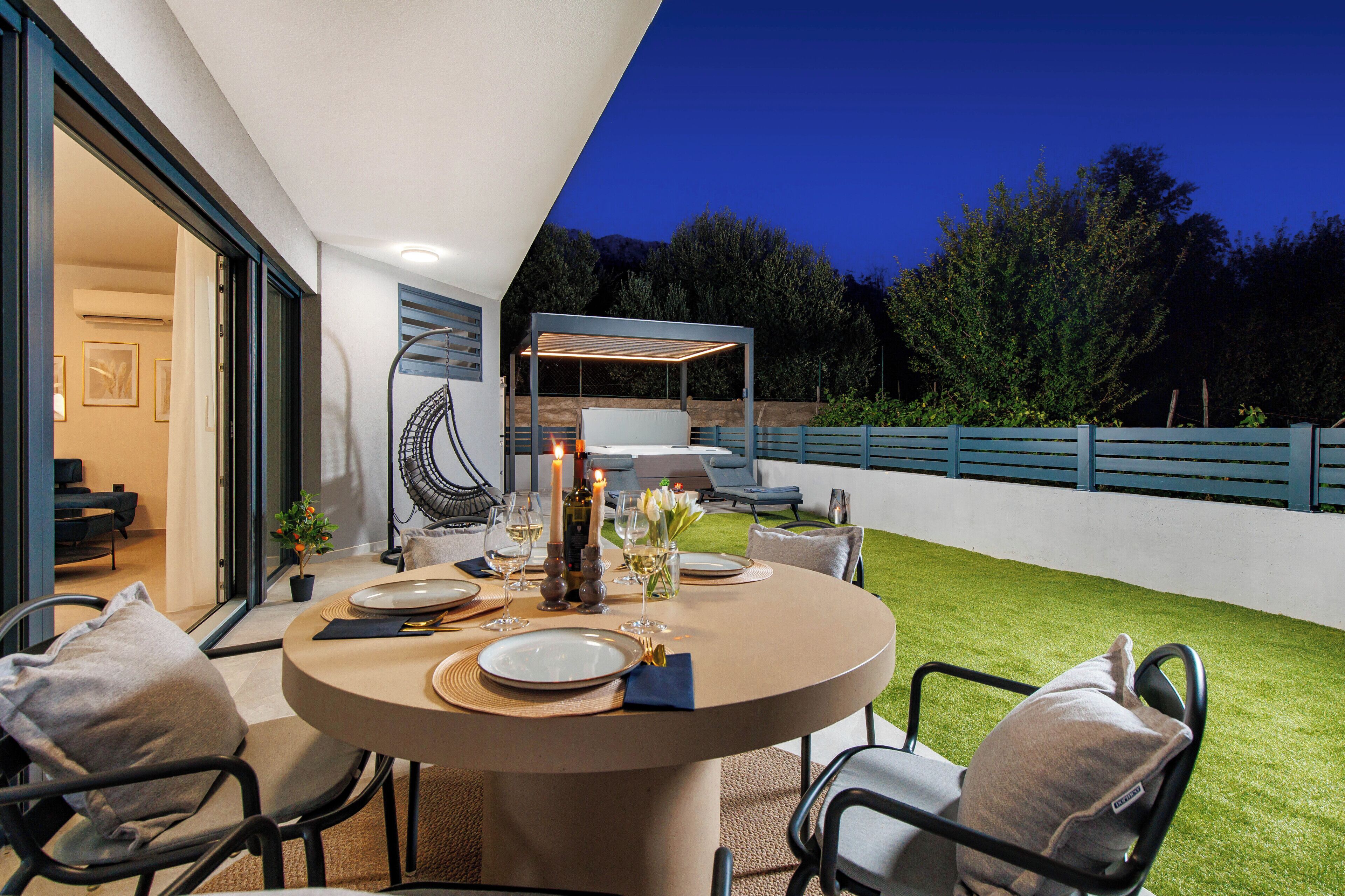 Un espace de restauration en plein air avec une table ronde, des chaises, des bougies et une vue sur le jardin et les arbres.