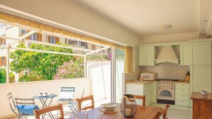 Een keuken met een magnetron, oven en kasten, een eettafel met stoelen en uitzicht op groen buiten.