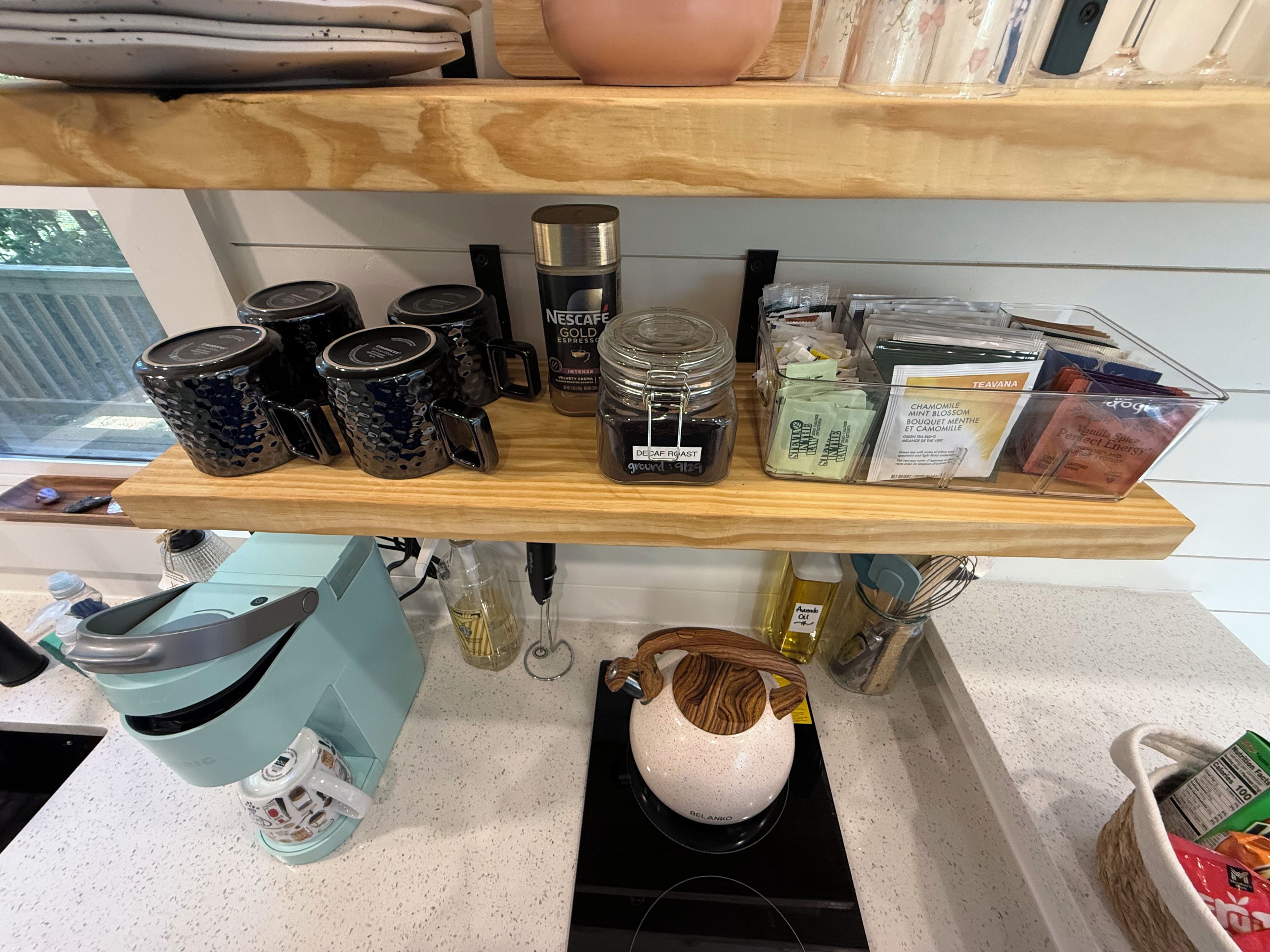 Un taulell de cuina amb diferents productes de cafè i te, incloent una màquina Nespresso, una exposició de te Teavana i una tetera Delanko.