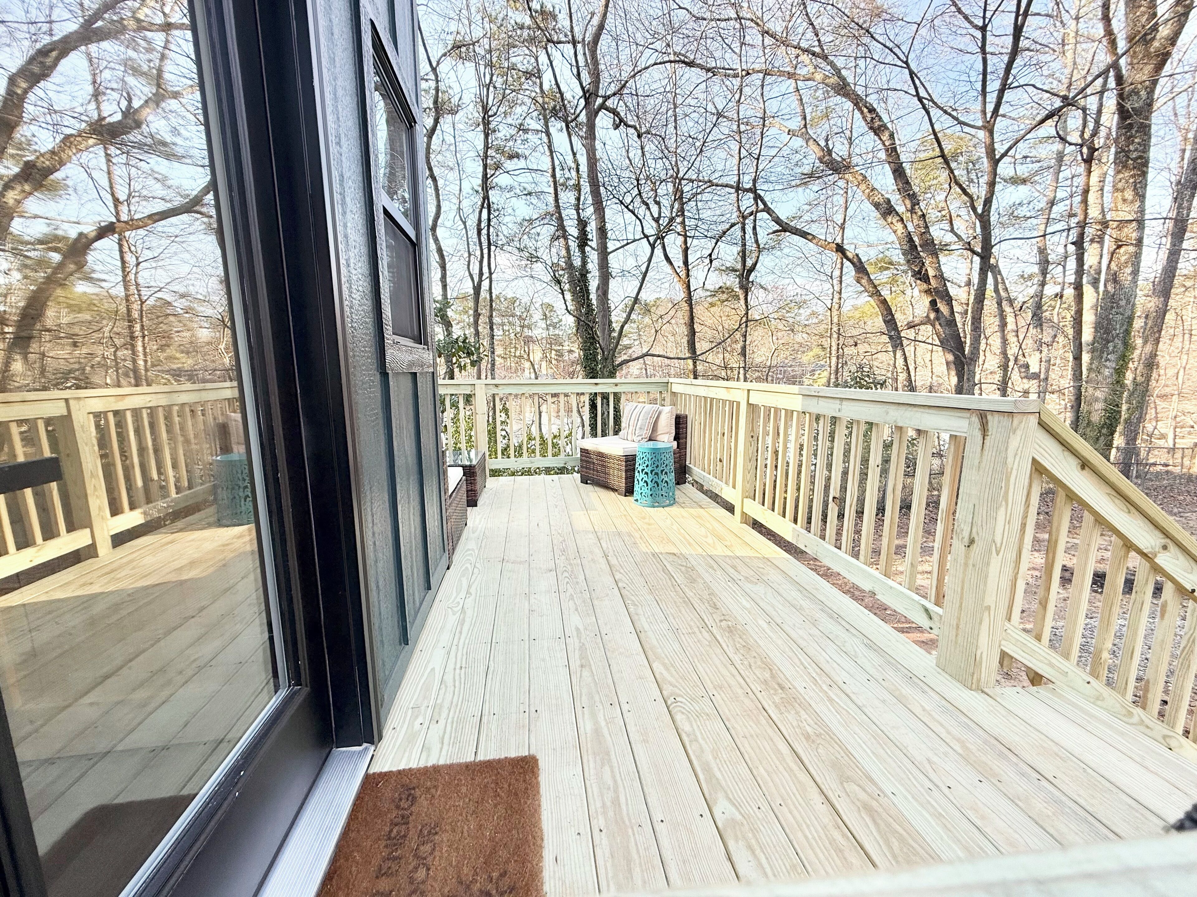 Une terrasse en bois offrant une vue sur les arbres, un banc en osier et une petite table.