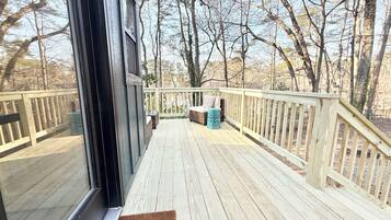 Une terrasse en bois offrant une vue sur les arbres, un banc en osier et une petite table.
