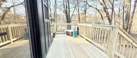Una terraza de madera con vistas a árboles, un banco de mimbre y una pequeña mesa.