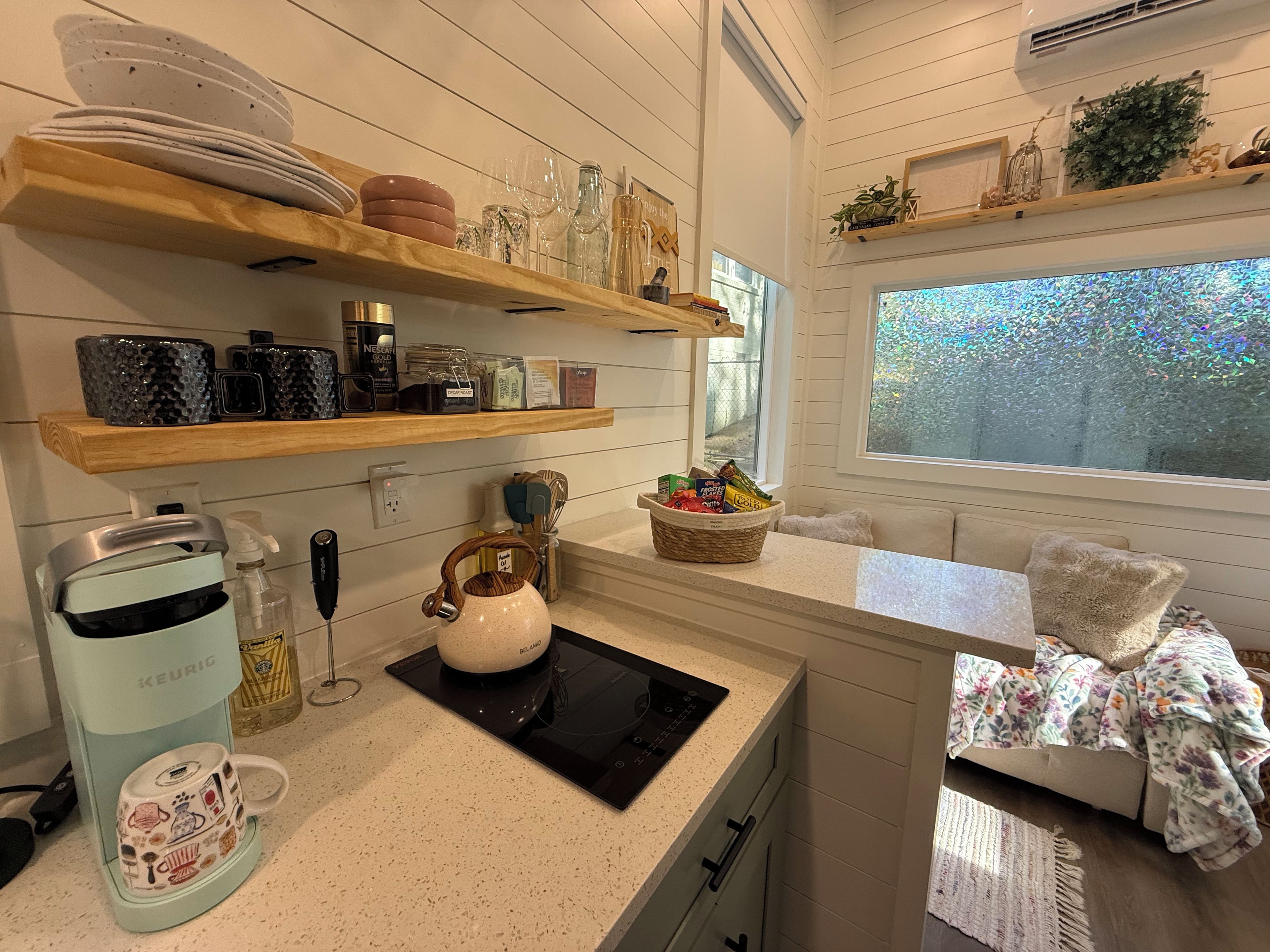 Una cocina con cafetera, hervidor y distintos utensilios de cocina en estantes.
