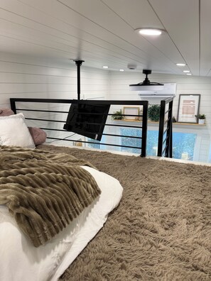 Ein Schlafzimmer mit Bett, Hängesessel, Deckenventilator und Blick auf einen Pool.
