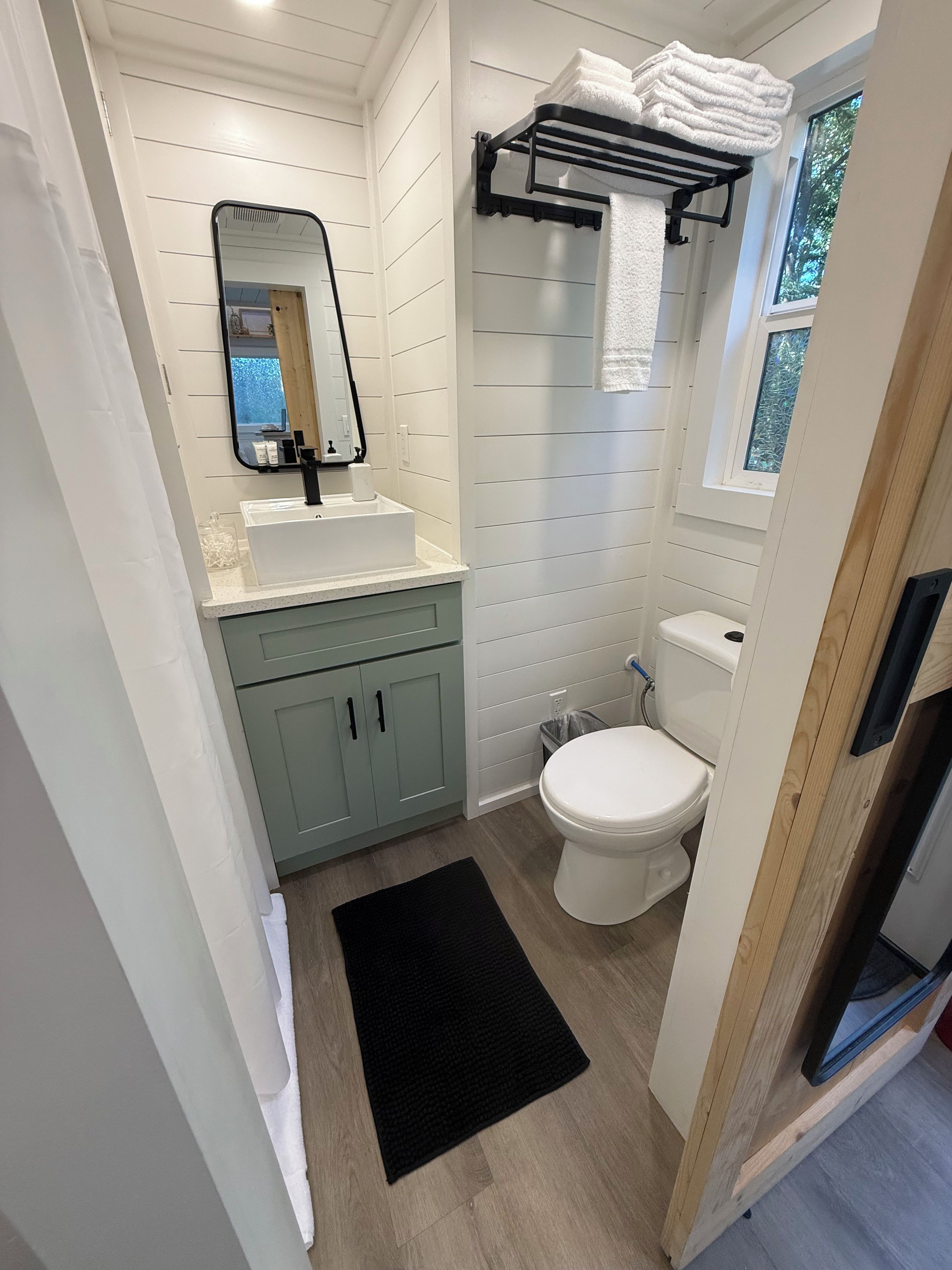 Et lille badeværelse med vask, spejl, toilet og håndklædestang.