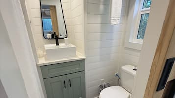 Et lille badeværelse med vask, spejl, toilet og håndklædestang.