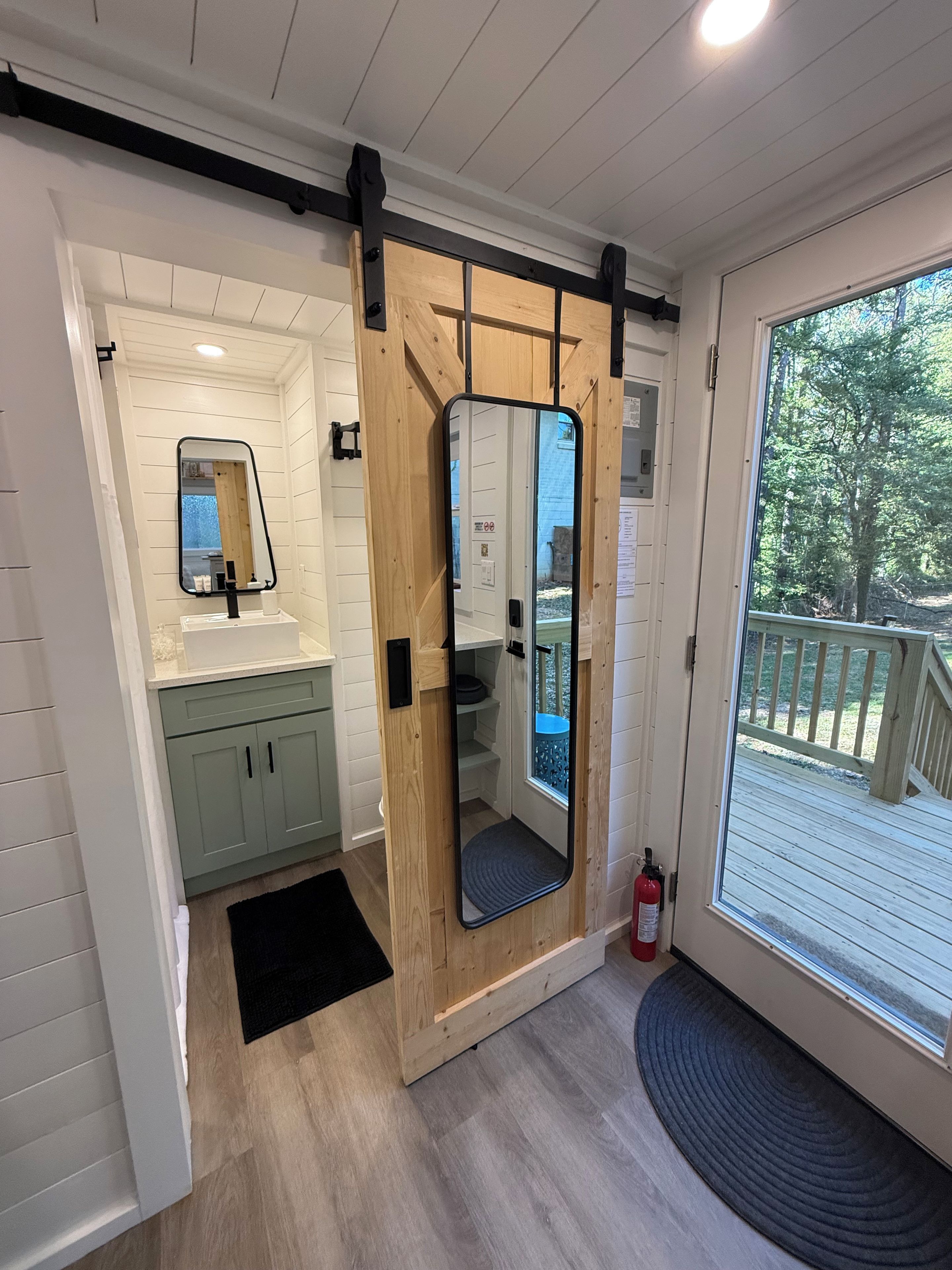 Un baño moderno con puerta de madera, un espejo grande y vistas a una terraza.