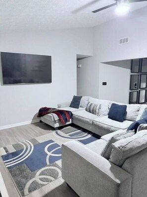 Ein modernes Wohnzimmer mit einem grauen Sofa, einem flachbildfernseher an der Wand und einem gemusterten Teppich.