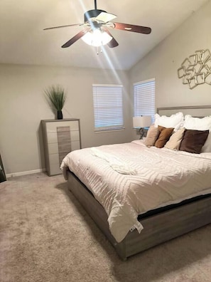 Ein Schlafzimmer mit Bett, Deckenventilator, Kommode und Wandleuchte.