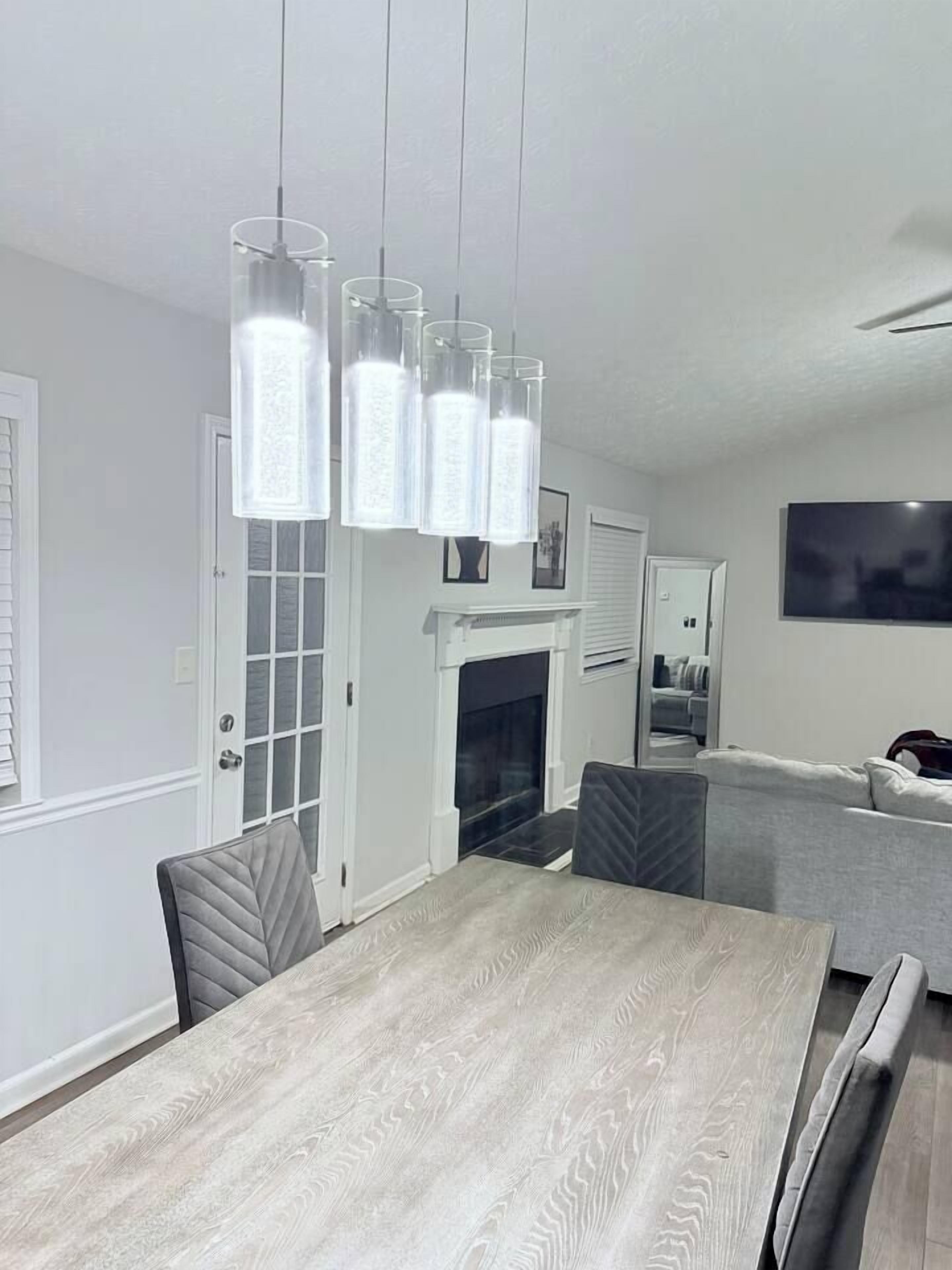A dining area with a wooden table and chairs, a fireplace, and a modern pendant light fixture.
