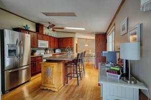 A kitchen with wooden cabinets, stainless steel appliances, a granite countertop, and a bar area with stools. - The Hoagie House - Family-Friendly Canal Home with Private Dock (Frankford)