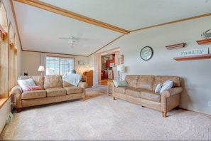 Ein geräumiges Wohnzimmer mit zwei Ledersofas, einem Deckenventilator und einer Uhr an der Wand.