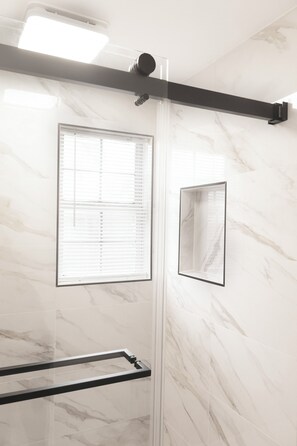 A bathroom with a glass shower enclosure, a towel rack, and a wall-mounted mirror.