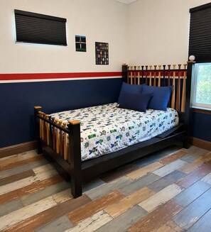 Un lit simple avec une couvre-lit à motifs, une tête de lit en bois et une bande rouge sur le mur.