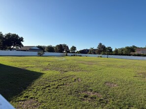 A grassy outdoor area with a white fence, trees, and houses in the background. - Cul-de-Sac Home – 1.28 acres – Tampa & Brandon (Dover)