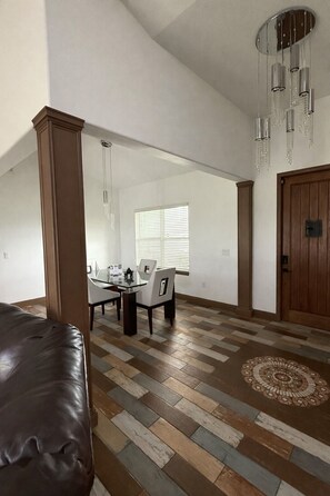 Un intérieur comprenant un coin repas, un canapé en cuir marron, un tapis à motifs et une porte en bois.