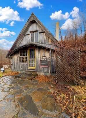 Ein rustikales Holzhaus mit einem pflasterbelagten Eingangsbereich, einem Holzzaun und blauem Himmel.