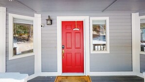 Ett hus med en röd dörr, två fönster och en veranda med en dörrmatta.