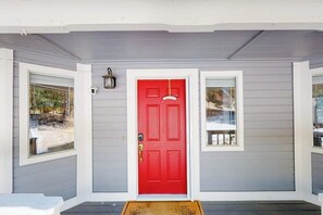 Ein Haus mit roter Tür, zwei Fenstern und einer Veranda mit Fußmatte.