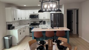 Una cocina moderna con armarios blancos, una isla central y un comedor con una mesa redonda y sillas.