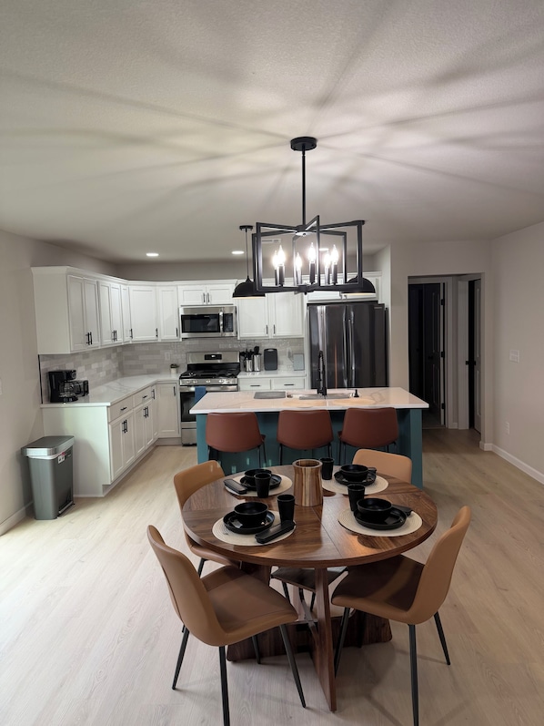 A modern kitchen with white cabinets, a central island, and a dining area with a round table and chairs.