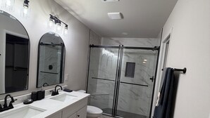 Un baño moderno con ducha envuelta en vidrio, un espejo grande y un tocador blanco.