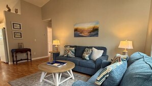 Ein Wohnzimmer mit einem blauen Sofa, einem Couchtisch, einem Deckenventilator und einem Bild an der Wand.