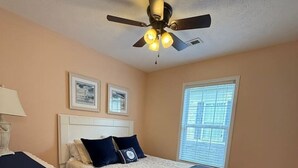 Ein Schlafzimmer mit Bett, Deckenventilator, Fenster und Schreibtisch.