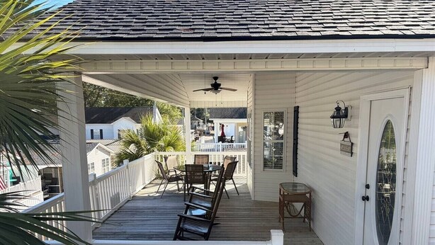Eine überdachte Veranda mit Tisch, Stühlen und einem Deckenventilator, sowie eine Tür mit Fensterglas.
