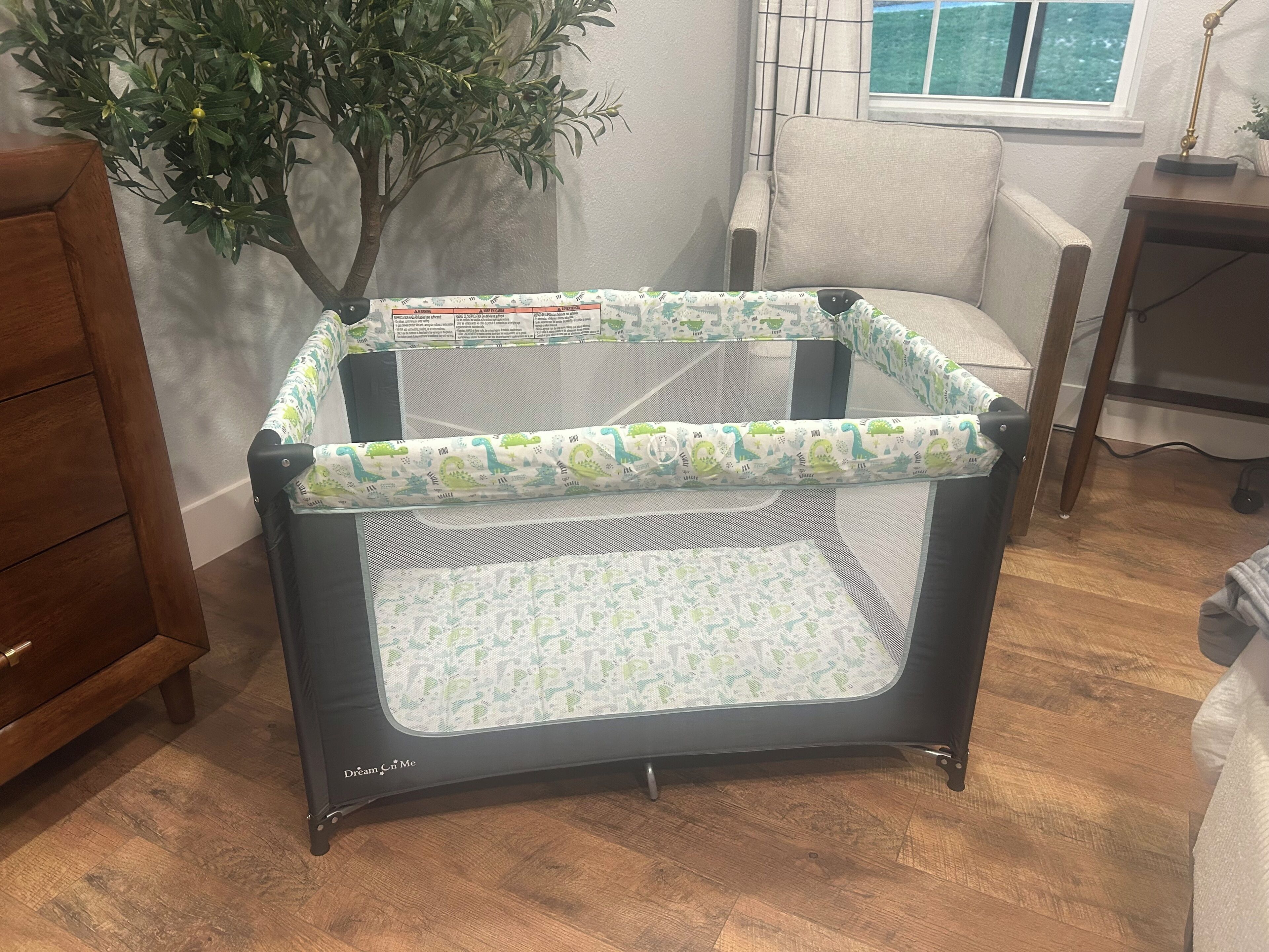 Ein Baby-Spielbereich mit dinosaurier-bezogener Stoffdecke, Holzboden, einem Fenster mit Vorhängen und einer Pflanze.